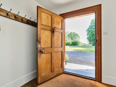 An open wooden front door showing a driveway and lawn outside with coat hooks on the interior wall at Bedingfield House nr Debenham Debenham