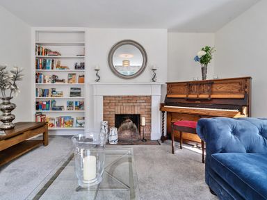 A living room with a brick fireplace a wooden piano a blue sofa and a bookshelf at Bedingfield House nr Debenham