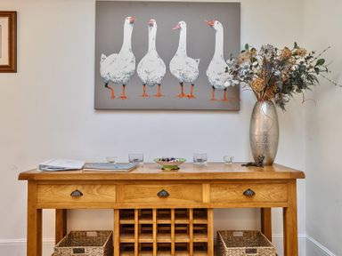 A wooden console table with drawers and baskets below a painting of five white geese at Bedingfield House nr Debenham