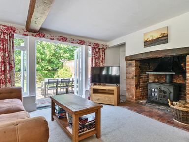 A living room with a brown sofa a wooden coffee table a television on a wooden stand an open doorway leading outside and a brick fireplace at Bedingfield House nr Debenham in Debenham