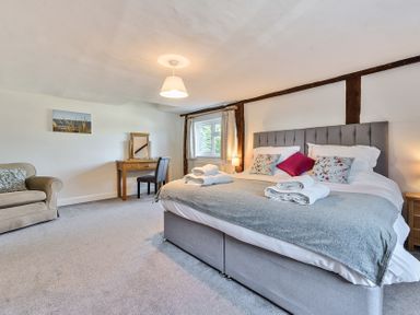 A bedroom with a large bed with folded towels bedside tables a window a desk with a chair and an armchair at Bedingfield House nr Debenham Debenham