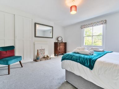 A bedroom with a bed covered with a teal blanket and rolled towels near window a wooden chest of drawers a teal chair and a white fireplace at Bedingfield House nr Debenham Debenham