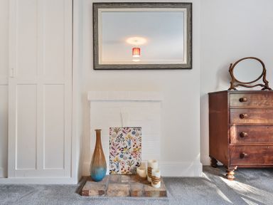 A room with a white painted fireplace decorated with a vase candles and a floral panel and a wooden dresser with a round mirror at Bedingfield House nr Debenham Debenham