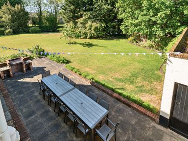 An outdoor patio with a long table and chairs near a brick barbecue and a lawn with trees in the background at Bedingfield House nr Debenham Debenham