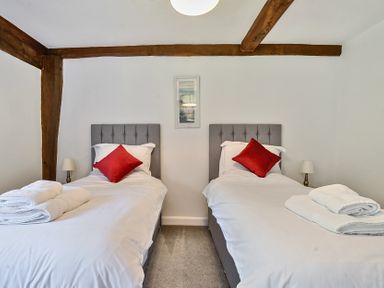 A bedroom with two single beds each with a red pillow and folded towels on a grey carpet at Bedingfield House nr Debenham Debenham