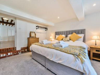 A bedroom with a double bed with yellow cushions and folded towels next to wooden bedside tables with lamps at Bedingfield House nr Debenham Debenham