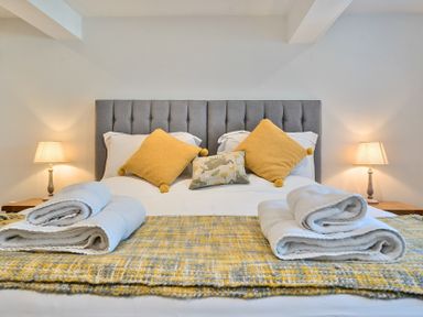 A bedroom with a gray upholstered headboard a bed with yellow and patterned pillows folded towels bedside lamps at Bedingfield House nr Debenham Debenham