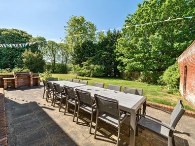 An outdoor patio with a long dining table and chairs near a brick barbecue in a garden at Bedingfield House nr Debenham Debenham