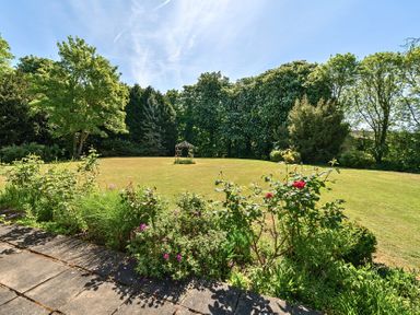 A garden with a stone patio and flower bushes overlooking a lawn and trees at Bedingfield House nr Debenham Debenham
