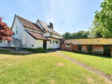 A white house with a tiled roof and an adjoining brick building with green doors in a grassy yard at Bedingfield House nr Debenham Debenham