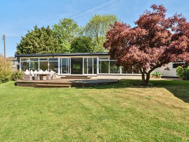 A garden with a grassy lawn a wooden deck seating area and a tree at Bedingfield House nr Debenham Debenham