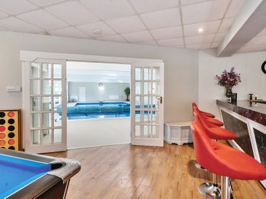 A recreational room with red bar stools a pool table and glass doors leading to an indoor swimming pool at Bedingfield House nr Debenham Debenham