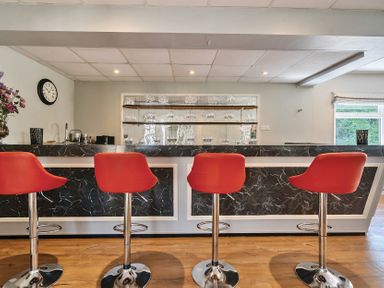 A bar area with four red bar stools wooden floor and glassware on shelves behind the counter at Bedingfield House nr Debenham Debenham