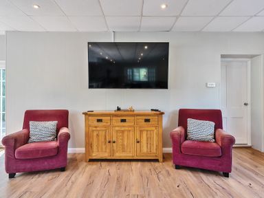 A living room with two red armchairs and a wooden cabinet beneath a wall-mounted television at Bedingfield House nr Debenham Debenham