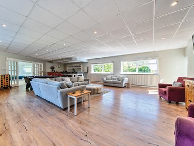 A large living room with grey sofas, a red armchair, a round ottoman, wooden flooring, and a bar area at Bedingfield House, nr Debenham in Debenham