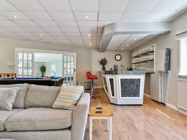 A room with a gray sofa, a bar counter with red stools, a pool table, and shelves with glassware at Bedingfield House nr Debenham Debenham