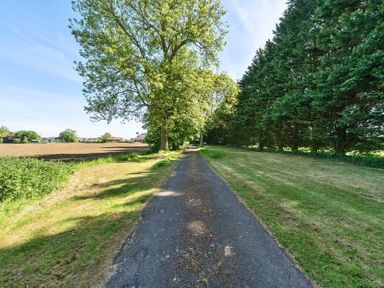 A paved pathway with green grass on both sides and trees lining the path at Bedingfield House nr Debenham Debenham