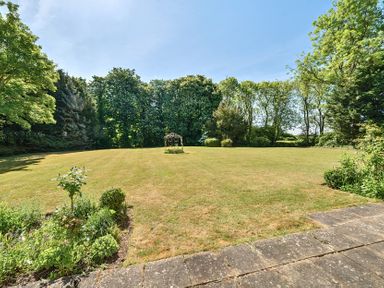 A large grassy garden with a metal gazebo structure in the center surrounded by trees and flower beds at Bedingfield House nr Debenham Debenham 