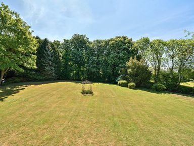 A large grassy garden with a metal garden structure and trees in the background at Bedingfield House nr Debenham Debenham