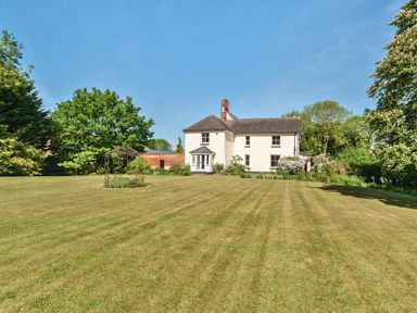 A large lawn with trees and shrubs surrounding a two-story white house at Bedingfield House nr Debenham in Debenham