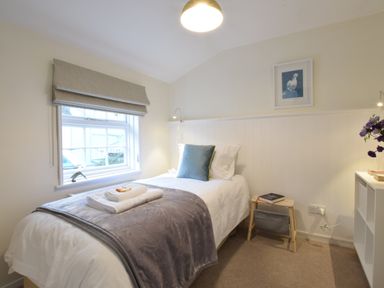 A small bedroom with a single bed by a window a bedside stool with books and a white shelf with flowers at Seaflower in Aldeburgh