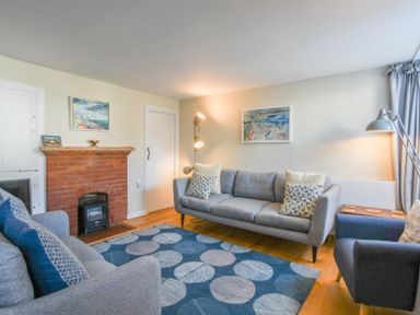 A living room with two grey sofas a blue armchair a blue rug with circular patterns a red brick fireplace and paintings on the wall at Seaflower Aldeburgh in Aldeburgh
