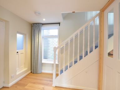 A hallway with wooden flooring a window with curtains a small door on the wall and a white staircase with blue steps at Seaflower Aldeburgh in Aldeburgh