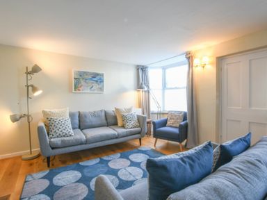 A living room with two gray sofas, a blue armchair, a floor lamp, a rug with circles, and a painting on the wall at Seaflower Aldeburgh in Aldeburgh