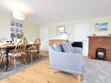 A dining table with six chairs and tableware next to a grey sofa and a brick fireplace in a living room at Seaflower Aldeburgh