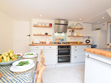 A kitchen with wooden countertops white cabinets a dining table with bowls of salad and a fruit bowl at Seaflower Aldeburgh