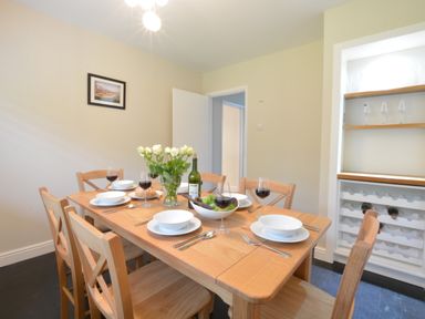 A dining room with a wooden table set for six people with white plates wine glasses and a vase of white flowers at Town Farm House Orford
