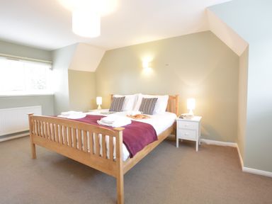 A bedroom with a wooden bed frame two bedside tables with lamps and a window at Town Farm House Orford