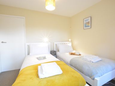A bedroom with two single beds white linens a yellow blanket folded towels on one bed and a breakfast tray on the other at Town Farm House Orford