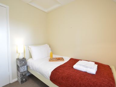 A single bed with white bedding red blanket and a tray with orange juice and croissants next to a small drawer unit with a lamp at Town Farm House Orford