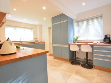 A kitchen with blue cabinets wooden countertops a white kettle two white chairs and a coffee maker at Town Farm House Orford