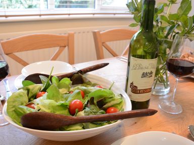 A dining table with a bowl of salad, a bottle of red wine, two wine glasses, and wooden chairs at Town Farm House Orford