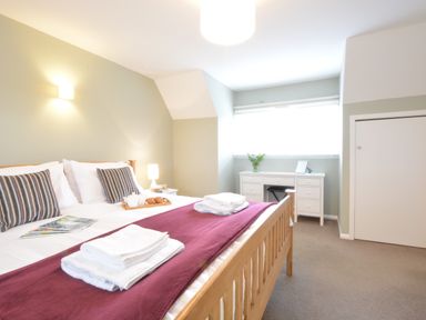 A bedroom with a wooden bed with white linens and striped pillows near a white desk with a chair at Town Farm House Orford