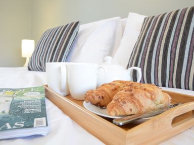 A breakfast tray with two croissants a teapot and two mugs on a bed with striped pillows and a magazine at Town Farm House Orford
