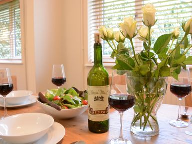 A dining table with a bottle of red wine glasses bowls a salad and a vase of white roses at Town Farm House Orford