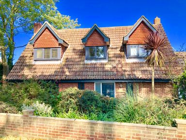 A house with a tiled roof and three dormer windows behind a brick wall and shrubs at Town Farm House Orford