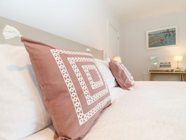 A bed with two pink patterned pillows and white bedding in a bedroom with a desk and lamps at Town Farm House Orford