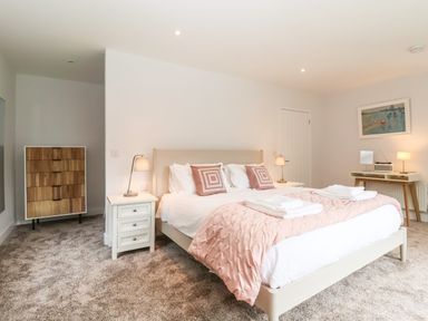 A bedroom with a bed with pink bedding two bedside tables with lamps a wooden chest of drawers and a desk with a lamp and mirror at Town Farm House Orford
