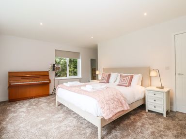 A bedroom with a bed a piano a window and two bedside tables with lamps at Town Farm House Orford