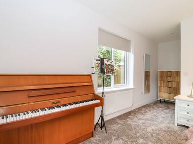 A room with a piano music stand a window a mirror a wooden chest of drawers and a white table at Town Farm House Orford