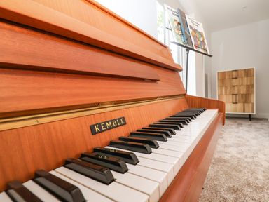 A wooden piano keyboard with sheet music on a stand and a wooden cabinet in a room at Town Farm House Orford