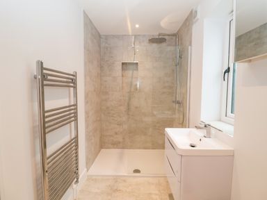 A bathroom with a walk-in shower a white sink unit a heated towel rail and a window at Town Farm House Orford