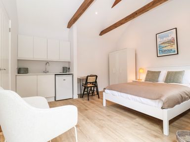 A bedroom with a bed a small kitchen area a desk with two chairs and a white armchair at Town Farm House Orford