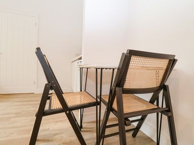 Two folding chairs with woven seats and backs at a small table in a room with wooden flooring at Town Farm House Orford