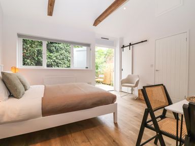 A bedroom with a bed brown blanket and pillows next to a window and door opening to a small outdoor area with chairs at Town Farm House Orford