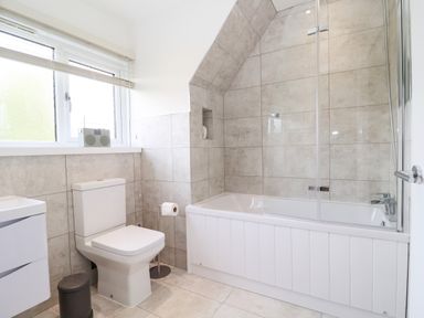 A bathroom with a toilet bathtub with glass shower screen window and sink at Town Farm House Orford